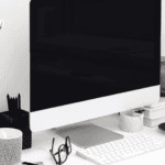 Modern workspace with computer, glasses, and decorative items in black and white.