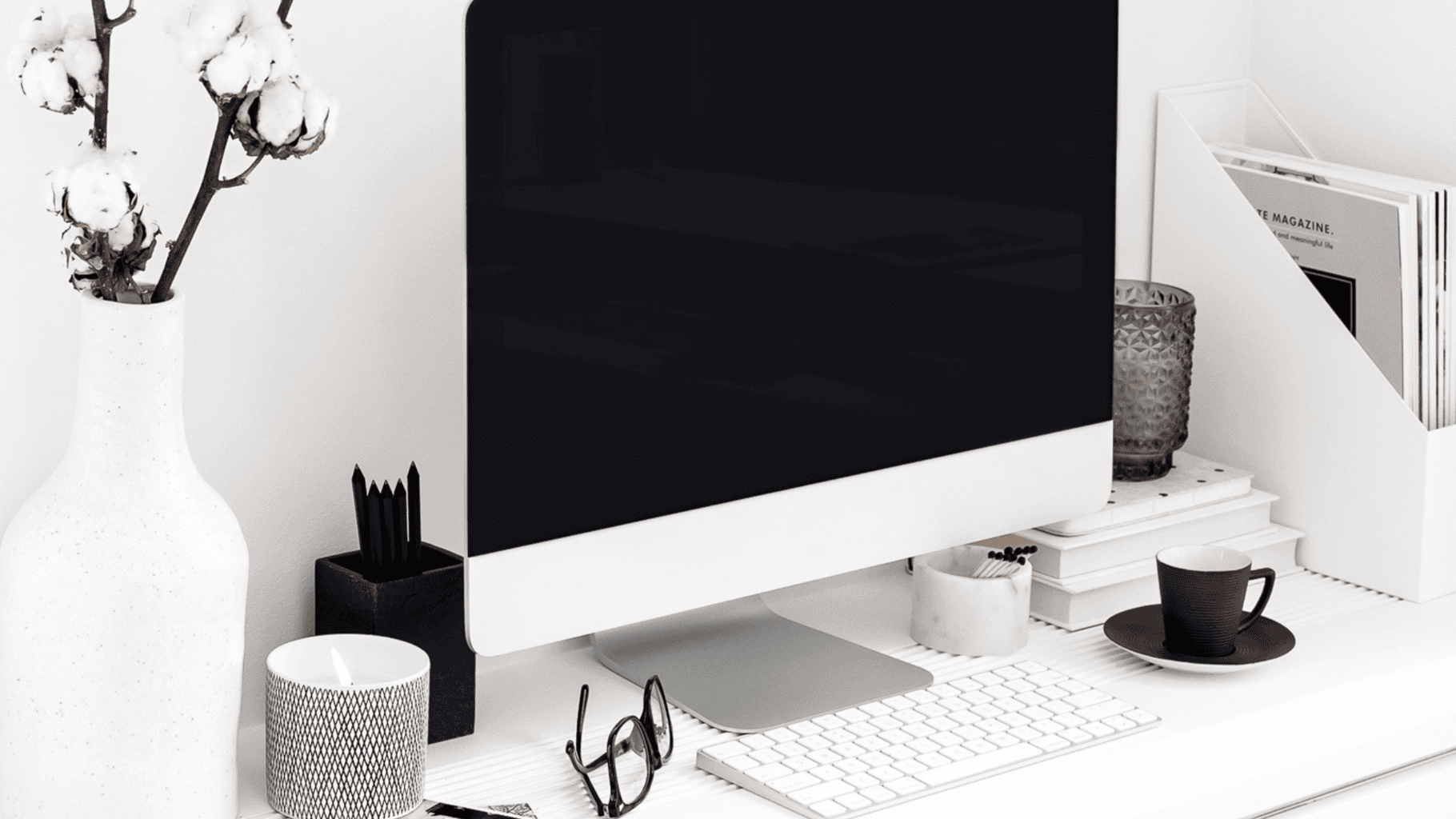 Modern workspace with computer, glasses, and decorative items in black and white.