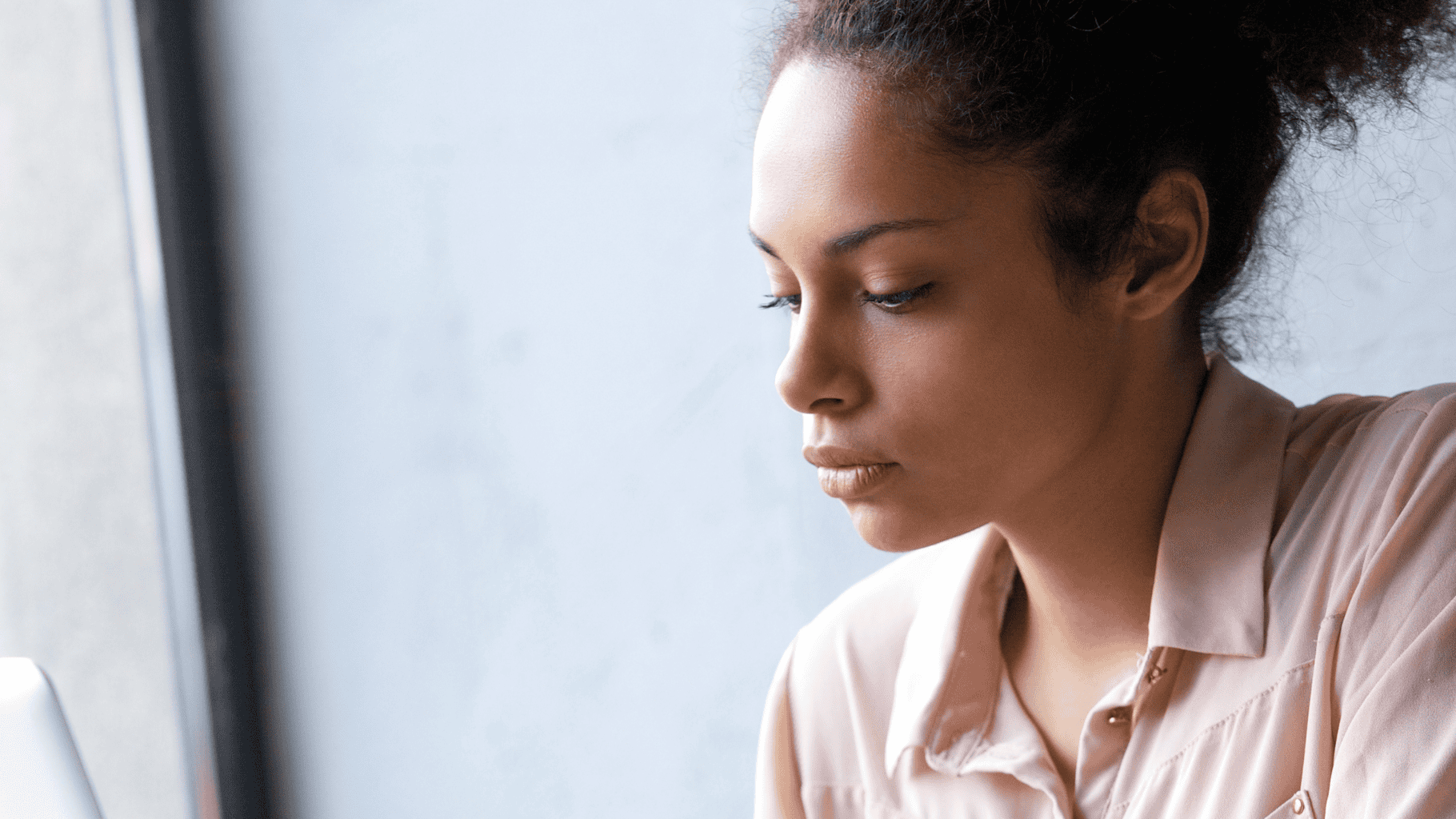 Contemplative woman in a neutral setting reflecting on her mood.