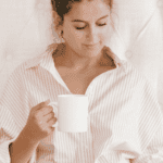 Woman holding a white coffee mug, looking down thoughtfully.