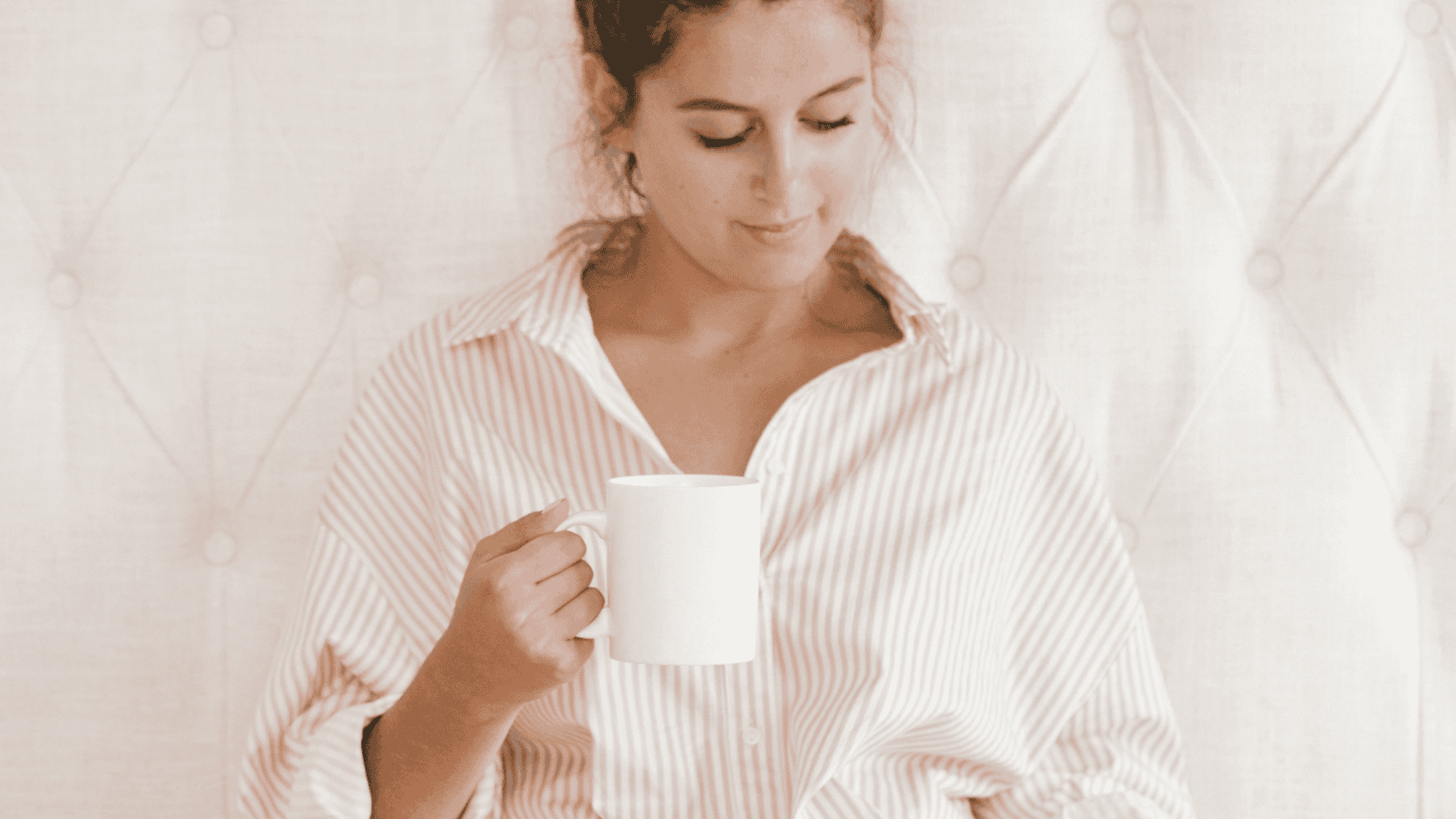 Woman holding a white coffee mug, looking down thoughtfully.