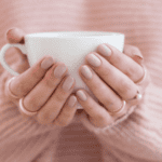 Person holding a white mug with both hands, wearing a pink sweater.