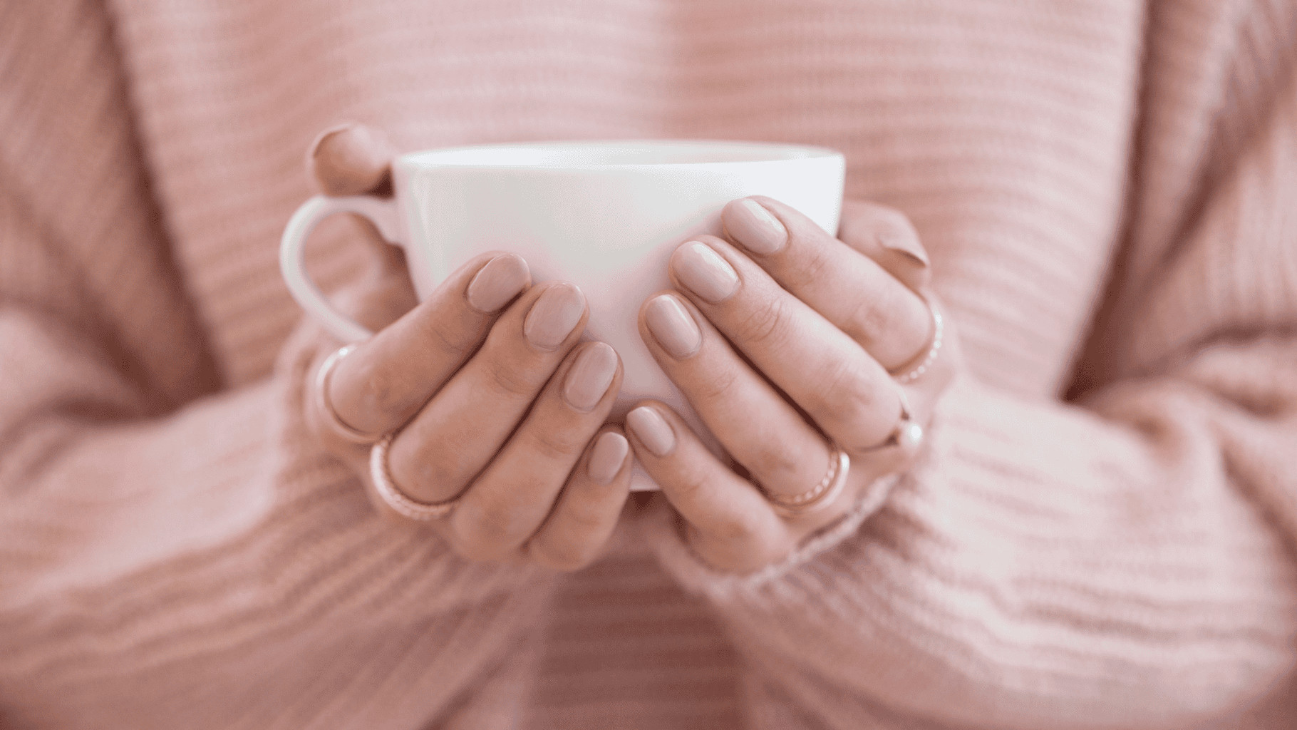 Person holding a white mug with both hands, wearing a pink sweater.