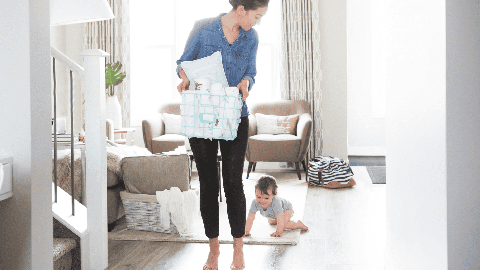 Mother carrying a diaper bag while playing with her crawling child at home.