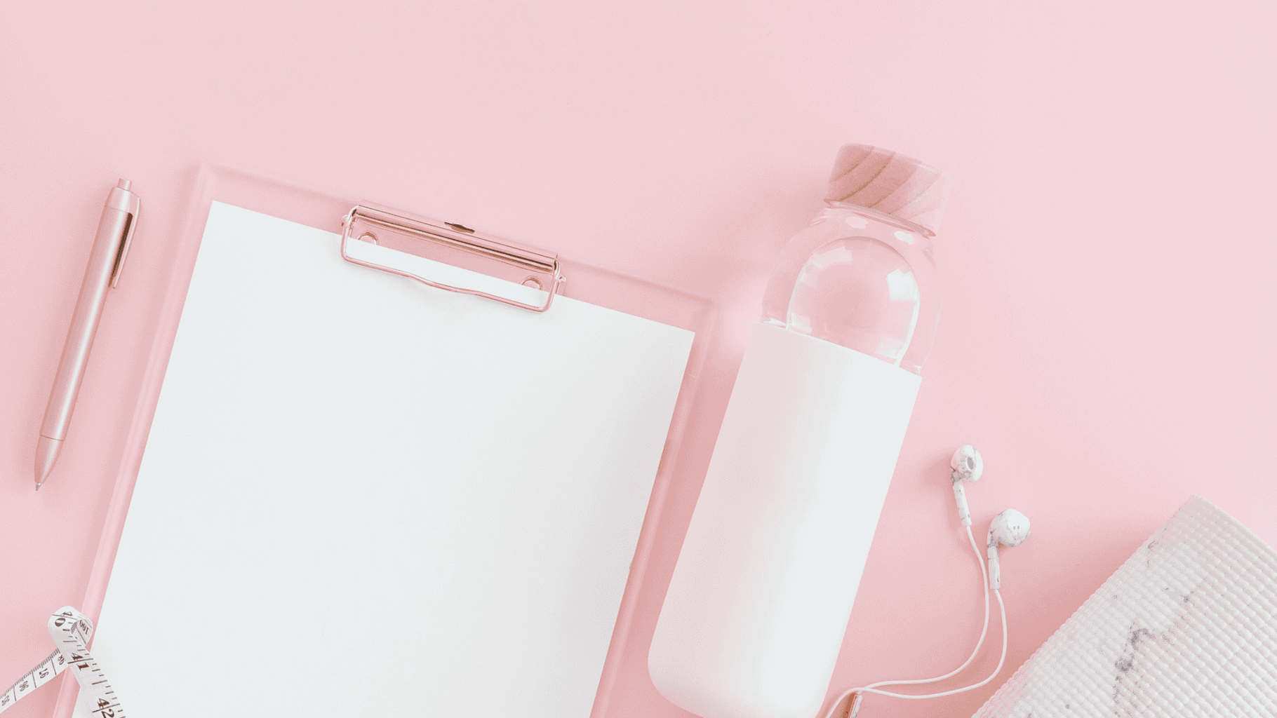 Clean pink workspace with notebook, water bottle, and earphones.