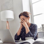 Woman feeling stressed and overwhelmed while working on her laptop at home.